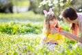 Cute little girl with curly hair wearing bunny ears and summer dress having fun with her young mother, relaxing in the garden Royalty Free Stock Photo