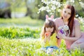Cute little girl with curly hair wearing bunny ears and summer dress having fun with her young mother, relaxing in the garden Royalty Free Stock Photo