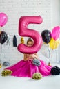 Cute little girl with dark hair, in a beautiful holiday dress and pink balloons for her birthday. The child is 5 years old. Holds Royalty Free Stock Photo