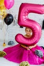 Cute little girl with dark hair, in a beautiful holiday dress and pink balloons for her birthday. The child is 5 years old. Holds Royalty Free Stock Photo