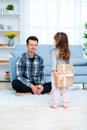 Cute little girl, daughter, sister gives a gift box to young dad father or brother. Both are smiling. Father`s day holiday concep