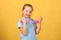 Cute little girl doing exercises with dumbbells in yellow background. Closeup portrait of sporty child with dumbbells Royalty Free Stock Photo