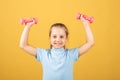 Cute little girl doing exercises with dumbbells in yellow background. Closeup portrait of sporty child with dumbbells Royalty Free Stock Photo