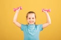 Cute little girl doing exercises with dumbbells in yellow background. Closeup portrait of sporty child with dumbbells Royalty Free Stock Photo