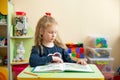 Cute little girl doing homework, reading a book, coloring pages, writing and painting. teaching in kindergarten Royalty Free Stock Photo