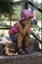 Cute little girl with doll sitting on the stone steps in a park Royalty Free Stock Photo