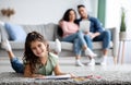 Cute Little Girl Drawing On Floor While Her Parents Relaxing On Couch Royalty Free Stock Photo