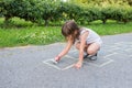 A cute little girl draws with chalk on the pavement in the park