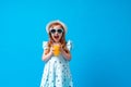 Cute little girl in a dress, hat and sunglasses poses on a blue background Royalty Free Stock Photo