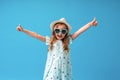 Cute little girl in a dress, hat and sunglasses poses on a blue background