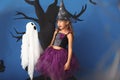 Cute little girl dressed as witch for Halloween and funny ghost against color wall with creepy decor Royalty Free Stock Photo