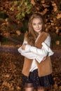 Cute little girl dressed in coat and boots sitting on autumn background