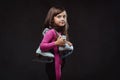 Cute little girl dressed in sportswear holds ice skates on a shoulder. Isolated on dark textured background. Royalty Free Stock Photo