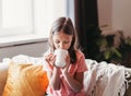 Cute little girl drinking tea at home on sofa Royalty Free Stock Photo