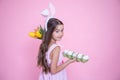 Cute little girl with easter bunny ears, a bouquet of flowers and a tray of easter eggs copy space