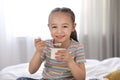 Cute little girl eating tasty yogurt on bed