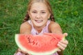 Cute little girl eating watermelon on the grass in summer time. with ponytail long hair and toothy smile sitting on grass and enjo Royalty Free Stock Photo