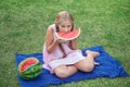 Cute little girl eating watermelon on the grass in summer time. with ponytail long hair and toothy smile sitting on grass and enjo Royalty Free Stock Photo