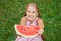 Cute little girl eating watermelon on the grass in summer time. with ponytail long hair and toothy smile sitting on grass and enjo Royalty Free Stock Photo