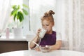 Cute little girl eats cereal with milk for Breakfast. The girl drinks milk from a glass glass. Healthy Breakfast, taking Royalty Free Stock Photo