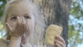 Cute little girl eats ice cream outside. Close-up portrait of blonde girl sitting on park bench and eating icecream Royalty Free Stock Photo