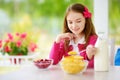 Cute little girl enjoying her breakfast at home. Pretty child eating corn flakes and raspberries and drinking milk before school. Royalty Free Stock Photo