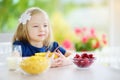 Cute little girl enjoying her breakfast at home. Pretty child eating corn flakes and raspberries and drinking milk before school. Royalty Free Stock Photo