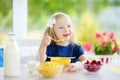 Cute little girl enjoying her breakfast at home. Pretty child eating corn flakes and raspberries and drinking milk before school. Royalty Free Stock Photo