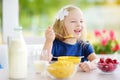 Cute little girl enjoying her breakfast at home. Pretty child eating corn flakes and raspberries and drinking milk before school. Royalty Free Stock Photo