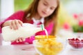 Cute little girl enjoying her breakfast at home. Pretty child eating corn flakes and raspberries and drinking milk before school. Royalty Free Stock Photo