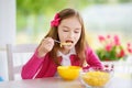 Cute little girl enjoying her breakfast at home. Pretty child eating corn flakes and raspberries and drinking milk before school. Royalty Free Stock Photo