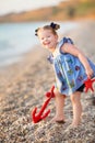 Cute little girl enjoying summer time on sea side beach happy playing with red star and tiny toy anchor on sand wearing nobby