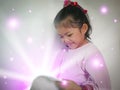 Cute little girl enjoys reading a magic book with light rays shining bright from  - read and education for a child Royalty Free Stock Photo