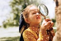 Cute little girl exploring the nature with magnifying glass outdoor. Child playing in the forest with magnifying glass. Curious Royalty Free Stock Photo
