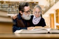 Cute little girl in eyeglasses sitting at the table in ancient library, hugging her grandfather and reading book Royalty Free Stock Photo