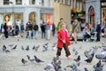 Cute little girl feeding and chasing birds on Dam Square in Amsterdam on summer day