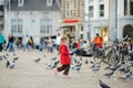 Cute little girl feeding and chasing birds on Dam Square in Amsterdam on summer day