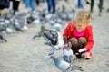 Cute little girl feeding and chasing birds on Dam Square in Amsterdam on summer day