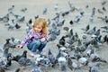 Cute little girl feeding and chasing birds on Dam Square in Amsterdam on summer day