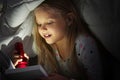 Cute little girl with flashlight reading book in bed under blanket Royalty Free Stock Photo