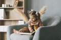 A cute little girl flips through a colorful educational book and sits in a chair in the room. Development, education