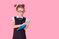 Cute little girl with glasses and books on pink background, space for text. Reading concept