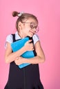 Cute little girl with glasses and books on pink background, space for text. Reading concept