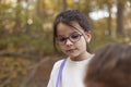 Cute little girl in glasses looking at her mother in autumn