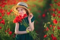 Cute little girl in green dress and straw hat with a bouquet of poppies posing at field of poppies in her hands on Royalty Free Stock Photo