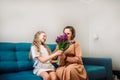 Cute little girl greeting her mother at home. Bouquet of purple tulips. Mother& x27;s day concept
