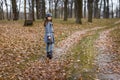 A cute little girl in grey coat and gray hat near the thick old oak in the oak wood at the sunset Royalty Free Stock Photo