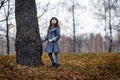 A cute little girl in grey coat and gray hat near the thick old oak in the oak wood at the sunset Royalty Free Stock Photo