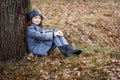 A cute little girl in grey coat and gray hat near the thick old oak in the oak wood at the sunset Royalty Free Stock Photo