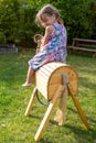 Cute little girl happily closing eyes when sitting on parents handmade wooden horse birthday present in garden. Royalty Free Stock Photo